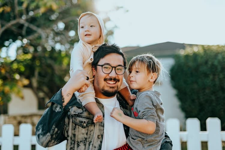 A smiling man holding two children